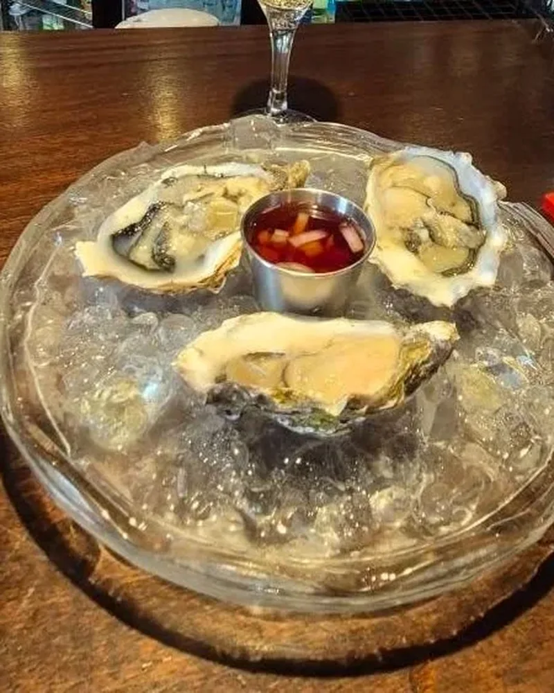 Oysters on ice with a dipping sauce and a glass of wine on the bar